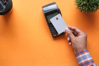 Hand houdt een betaalkaart bij een pinautomaat op een oranje ondergrond