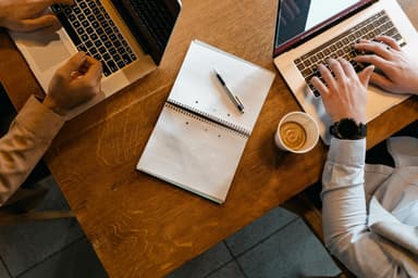 Bovenaanzicht van een tafel met laptops, aantekeningen en koffie