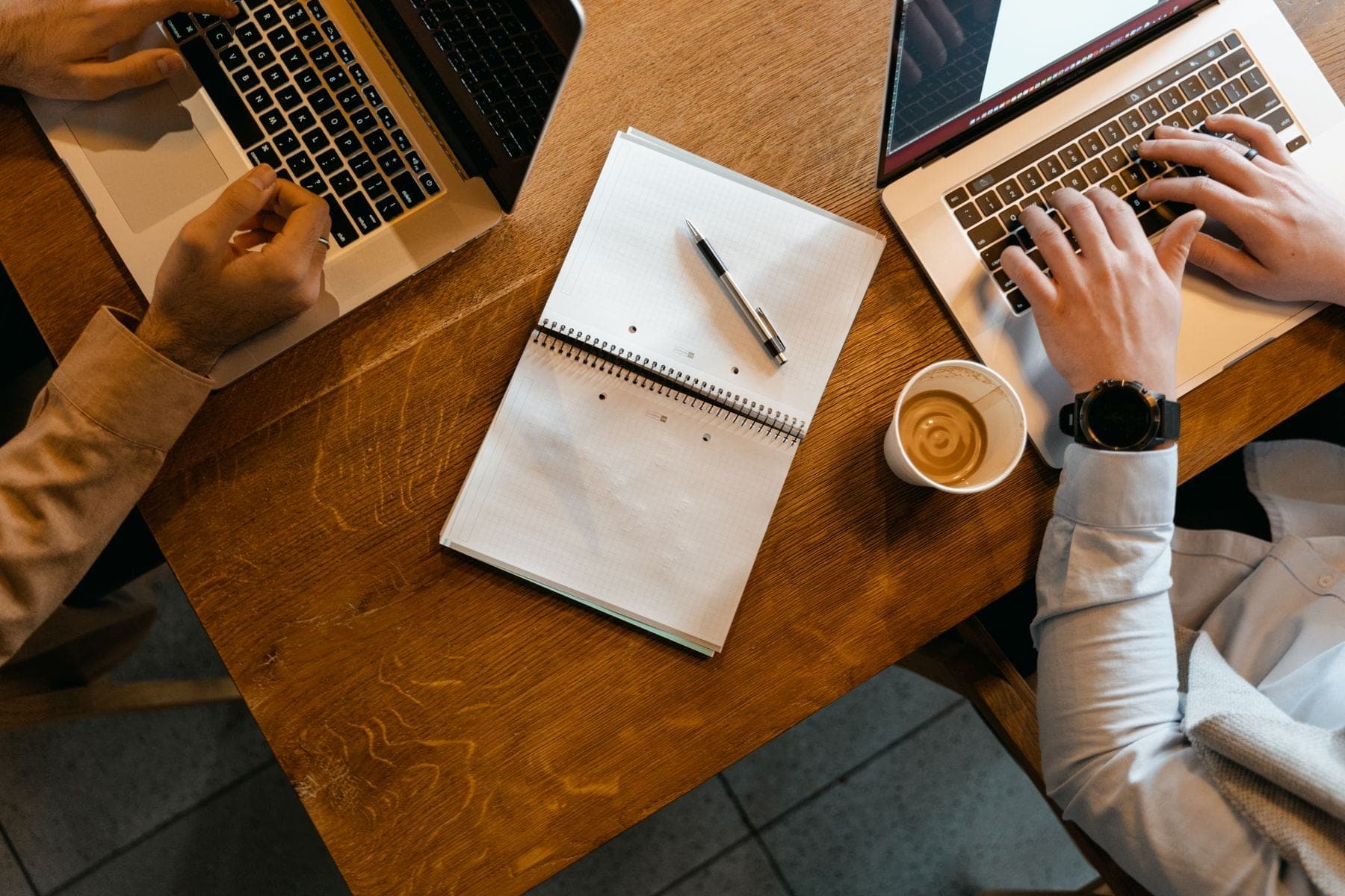 Bovenaanzicht van een tafel met laptops, aantekeningen en koffie