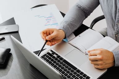 Iemand bekijkt financiële documenten naast een laptop