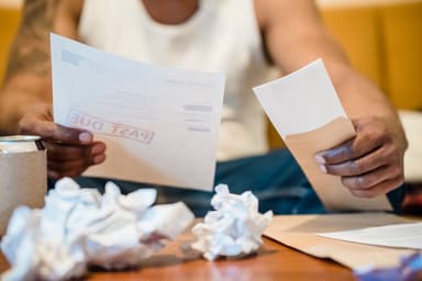 Handen met achterstallige rekeningen en verfrommeld papier op tafel