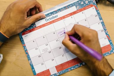 Hand schrijft een afspraak op een maandkalender