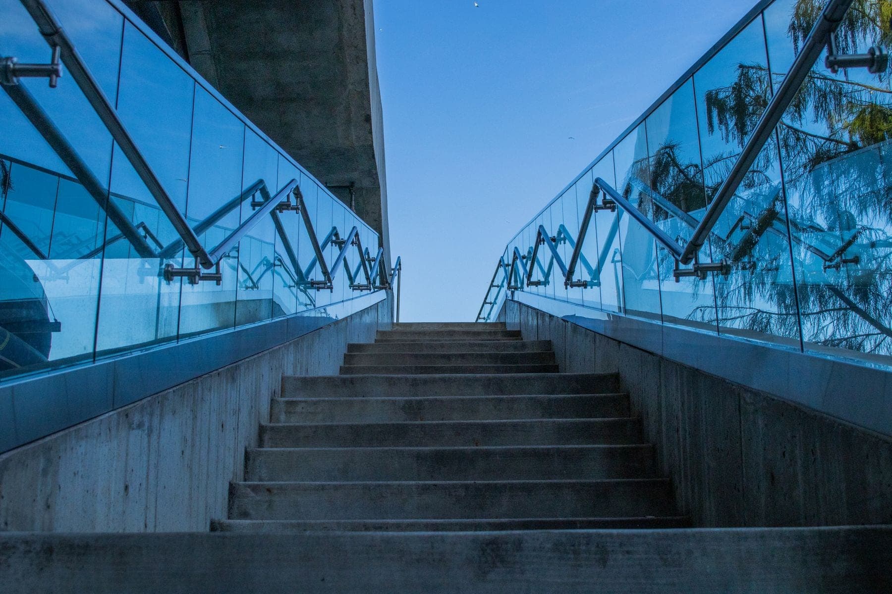 Betonnen trap met glazen leuningen naar een blauwe lucht
