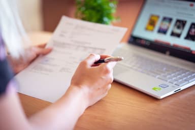 Hand vergelijkt een brief met de gegevens op een laptop