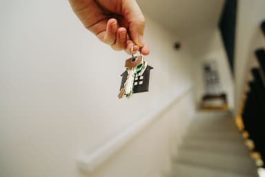 Hand overhandigt huissleutels met een huisvormige sleutelhanger