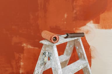 Verfroller op een trap voor een half geverfde muur