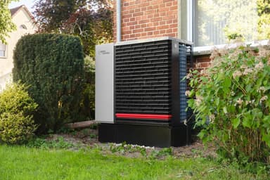 Buitenunit van een warmtepomp naast een woning