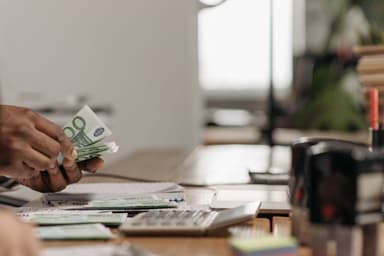 Handen tellen eurobiljetten boven een bureau met een rekenmachine en papieren