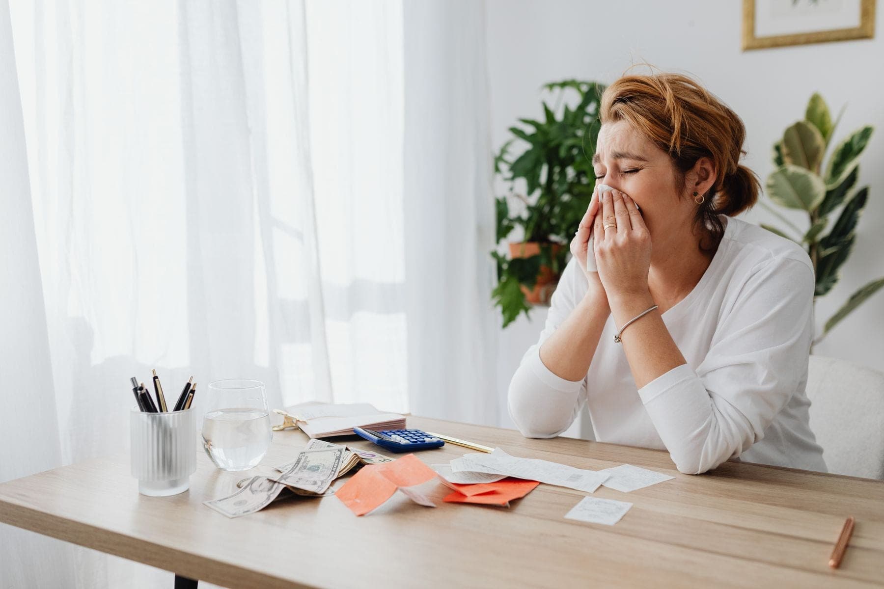 Vrouw aan haar bureau met papieren en een rekenmachine kijkt bezorgd naar haar financiën