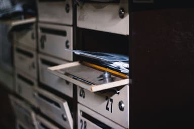 Een geopende brievenbus met post erin, tussen rijen gesloten brievenbussen in een portiek