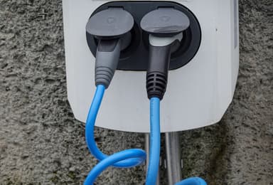Twee blauwe laadkabels aangesloten op een laadpunt aan een grijze muur