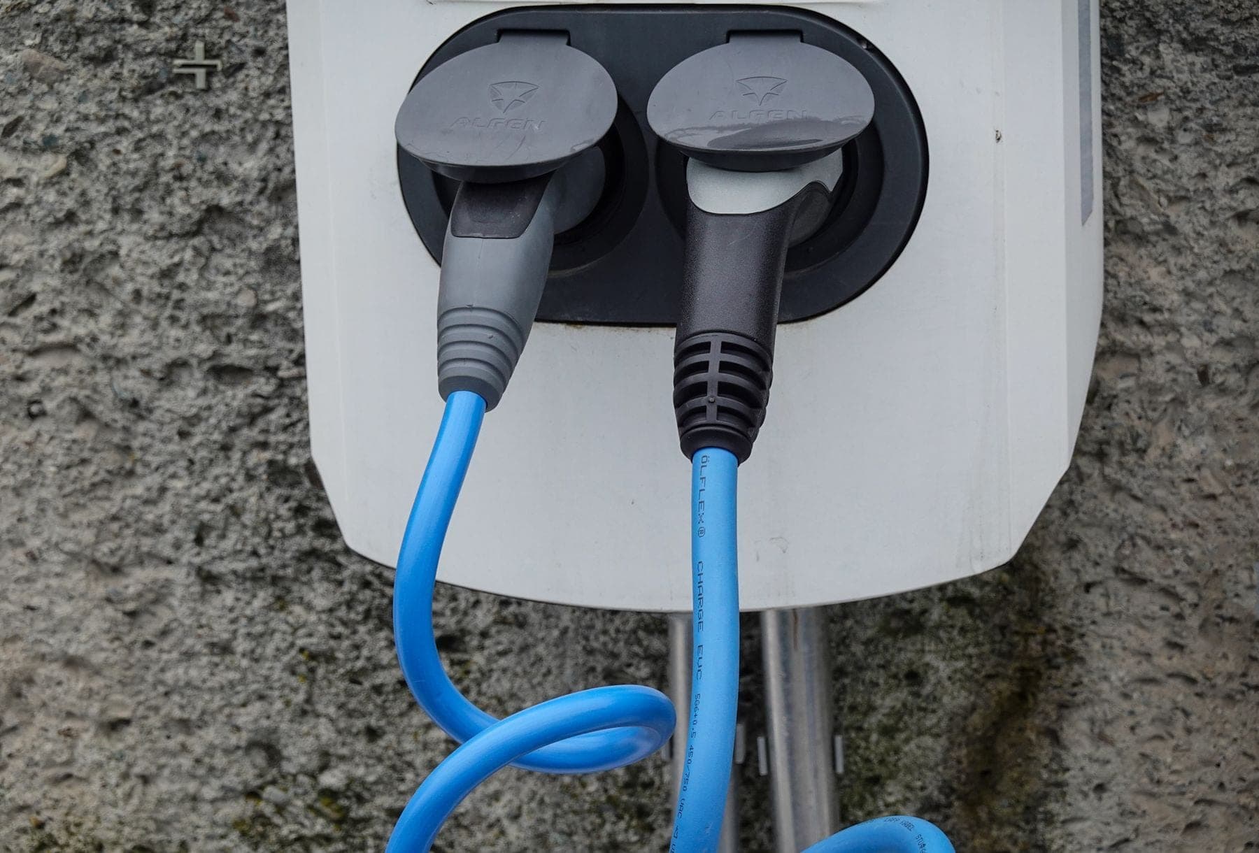 Twee blauwe laadkabels aangesloten op een laadpunt aan een grijze muur