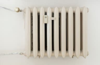 Klassieke witte radiator tegen een lichte, kale muur in een woning