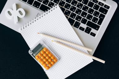 Rekenmachine, notitieblok en potloden naast een laptop, met een procentteken