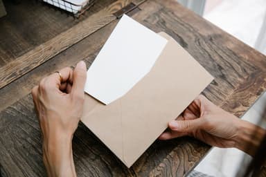 Twee handen halen een blanco brief uit een bruine envelop boven een houten tafel