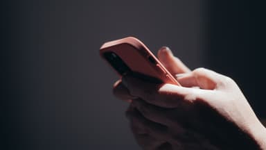 Twee handen houden een rode smartphone vast in een donkere ruimte