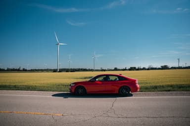 Rode auto op een landweg langs een graanveld met windmolens in de verte