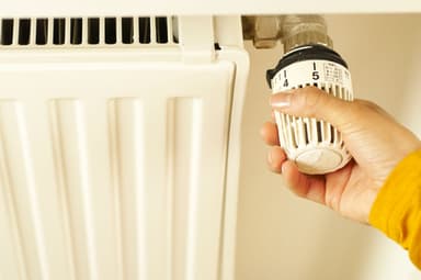 Een hand draait aan de thermostaatknop van een witte radiator