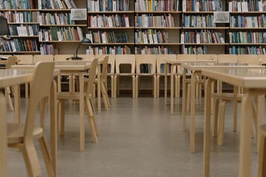 Lege houten tafels en stoelen in een universiteitsbibliotheek met volle boekenkasten