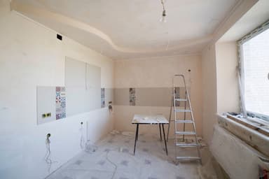 Een keuken in verbouwing met een trapladder, een werktafel en kale, deels betegelde muren