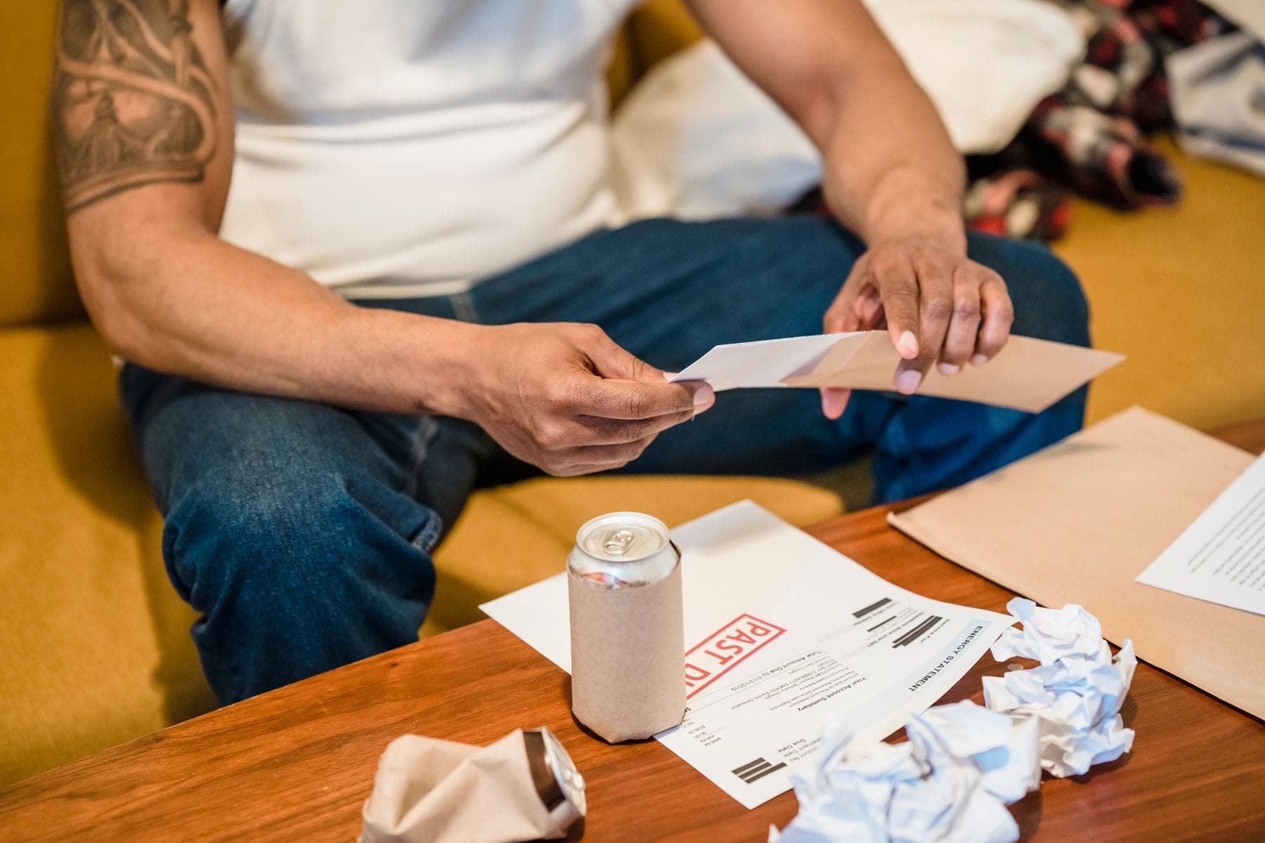 Een man op de bank bekijkt zijn post, met enveloppen en papieren om zich heen