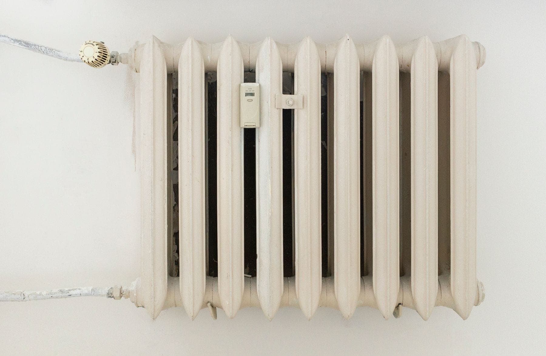 Klassieke witte radiator tegen een lichte, kale muur in een woning
