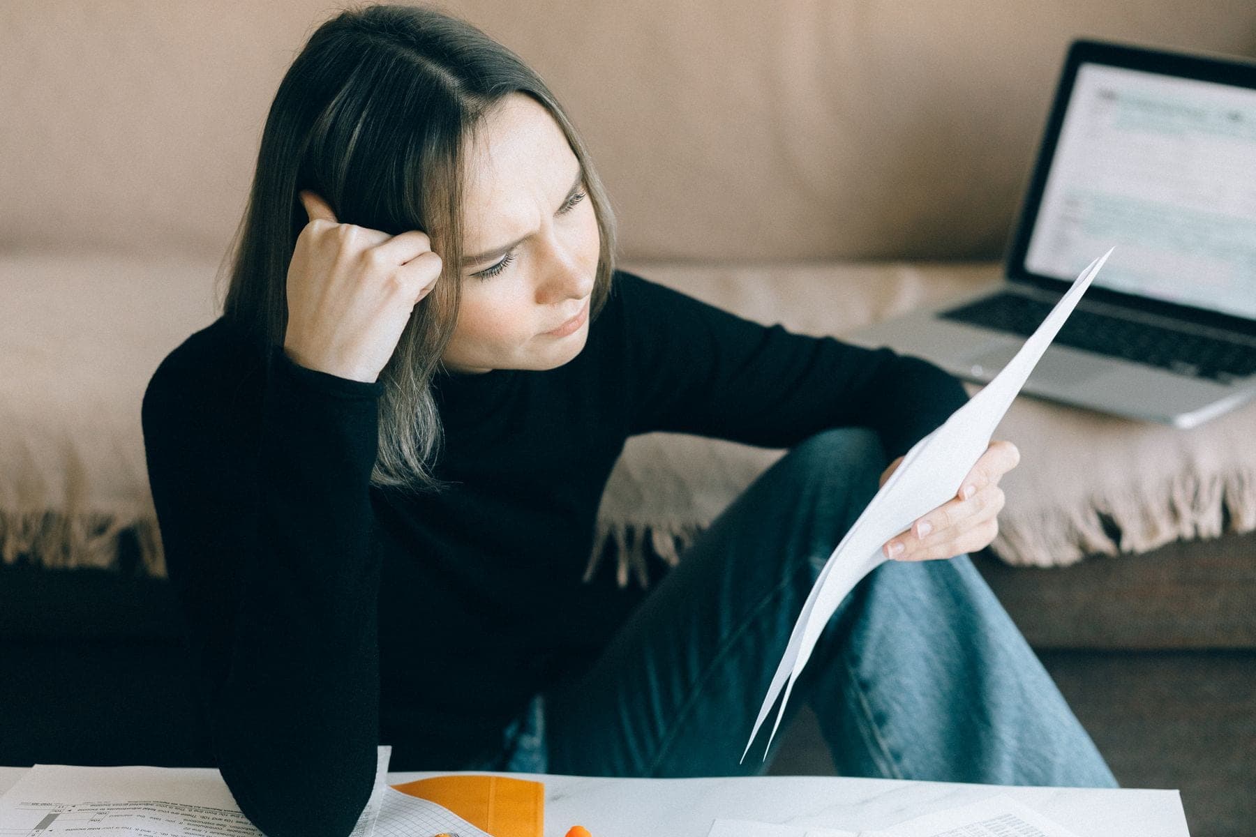 Vrouw vergelijkt papieren naast een open laptop aan tafel