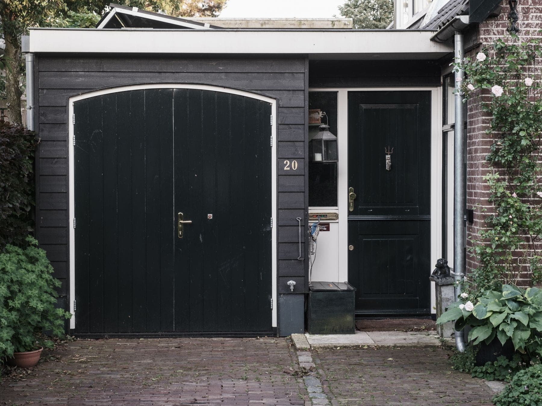 Voorgevel van een huis met zwarte houten garagedeuren, een zwarte voordeur en een oprit van klinkers