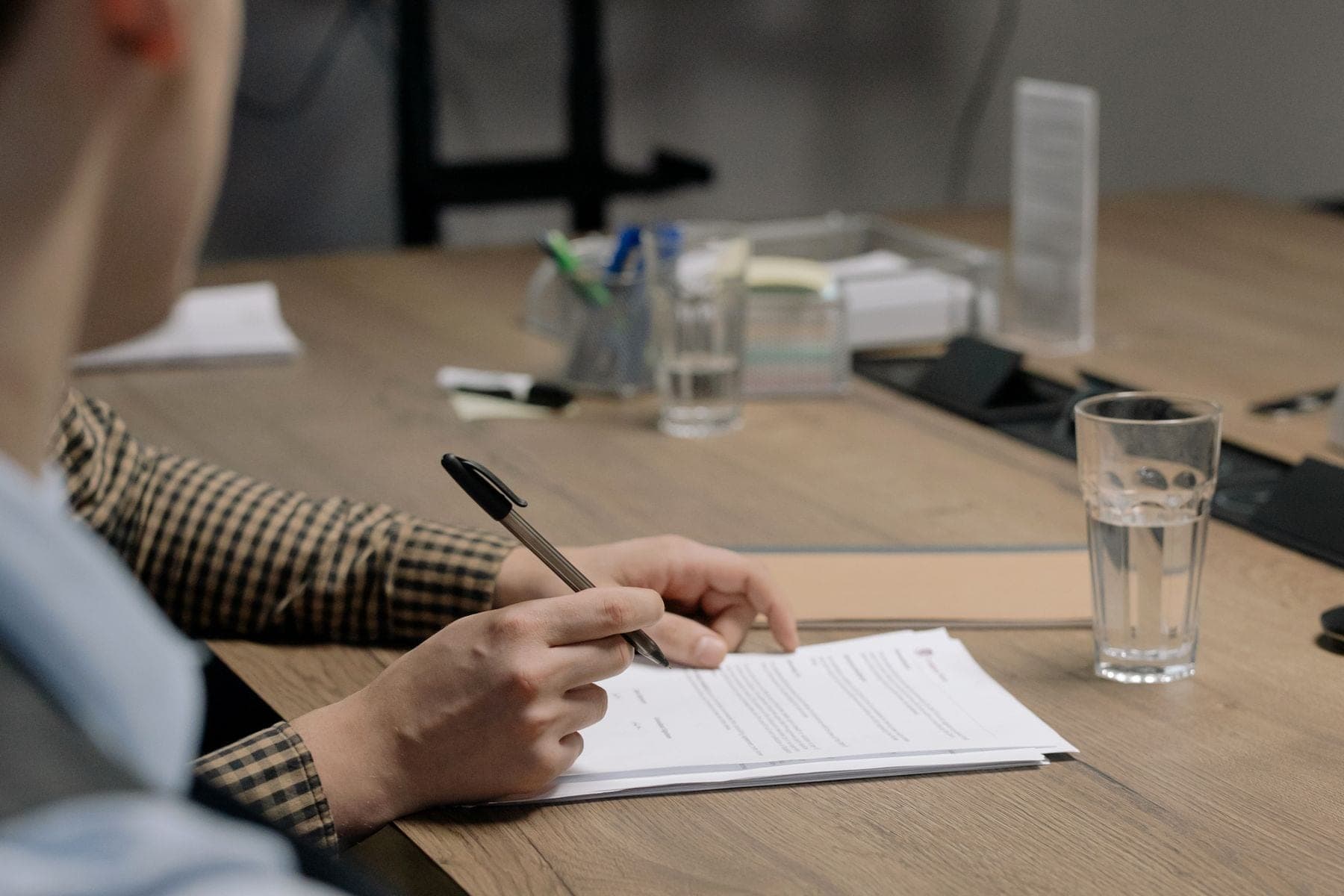 Iemand zet met een pen een handtekening onder een document aan een houten vergadertafel