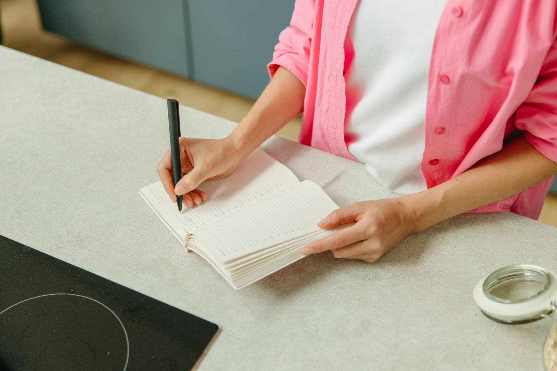 Vrouw schrijft met een pen in een notitieboek aan het aanrecht in de keuken