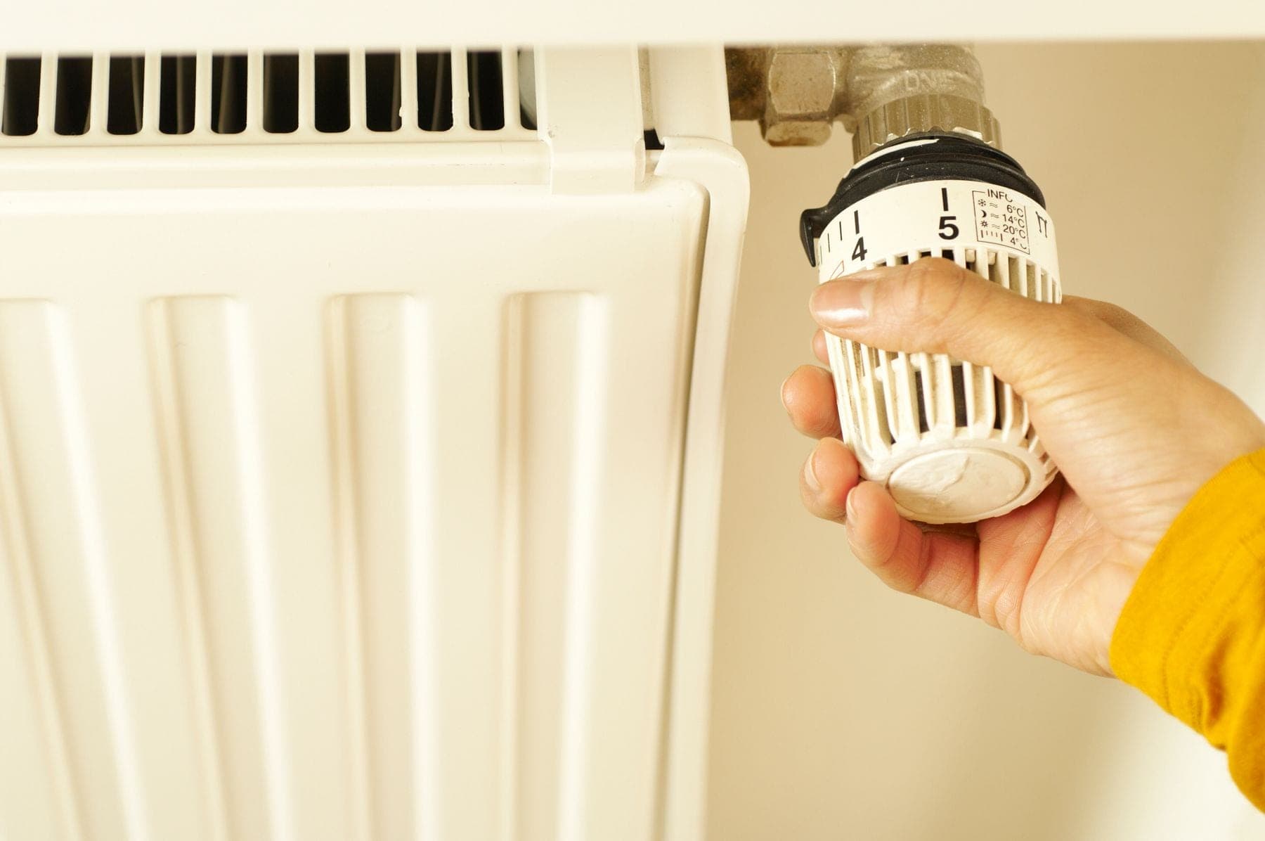 Een hand draait aan de thermostaatknop van een witte radiator