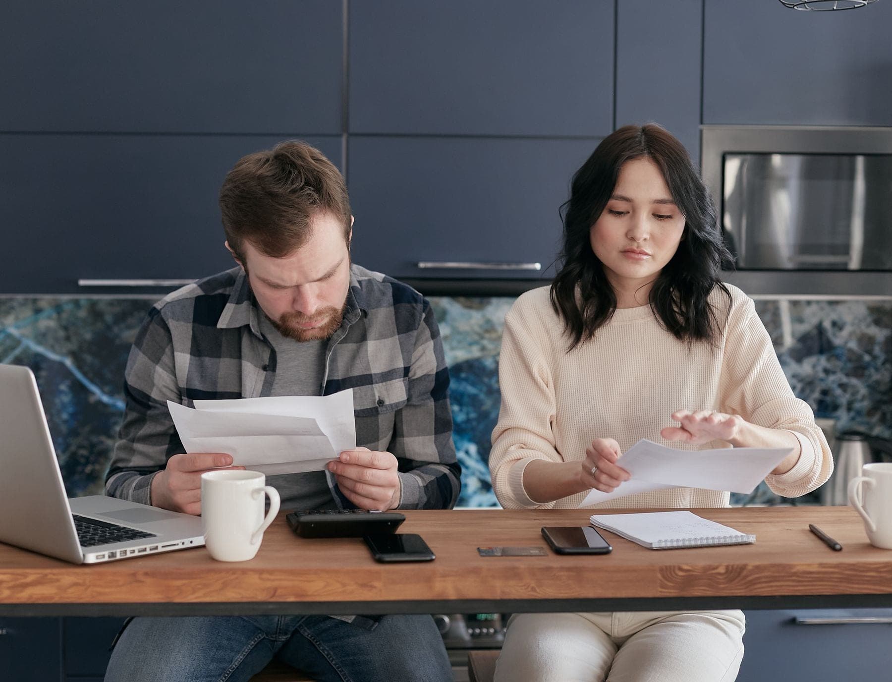 Een man en een vrouw lezen elk een brief aan de keukentafel, met een laptop en koffie