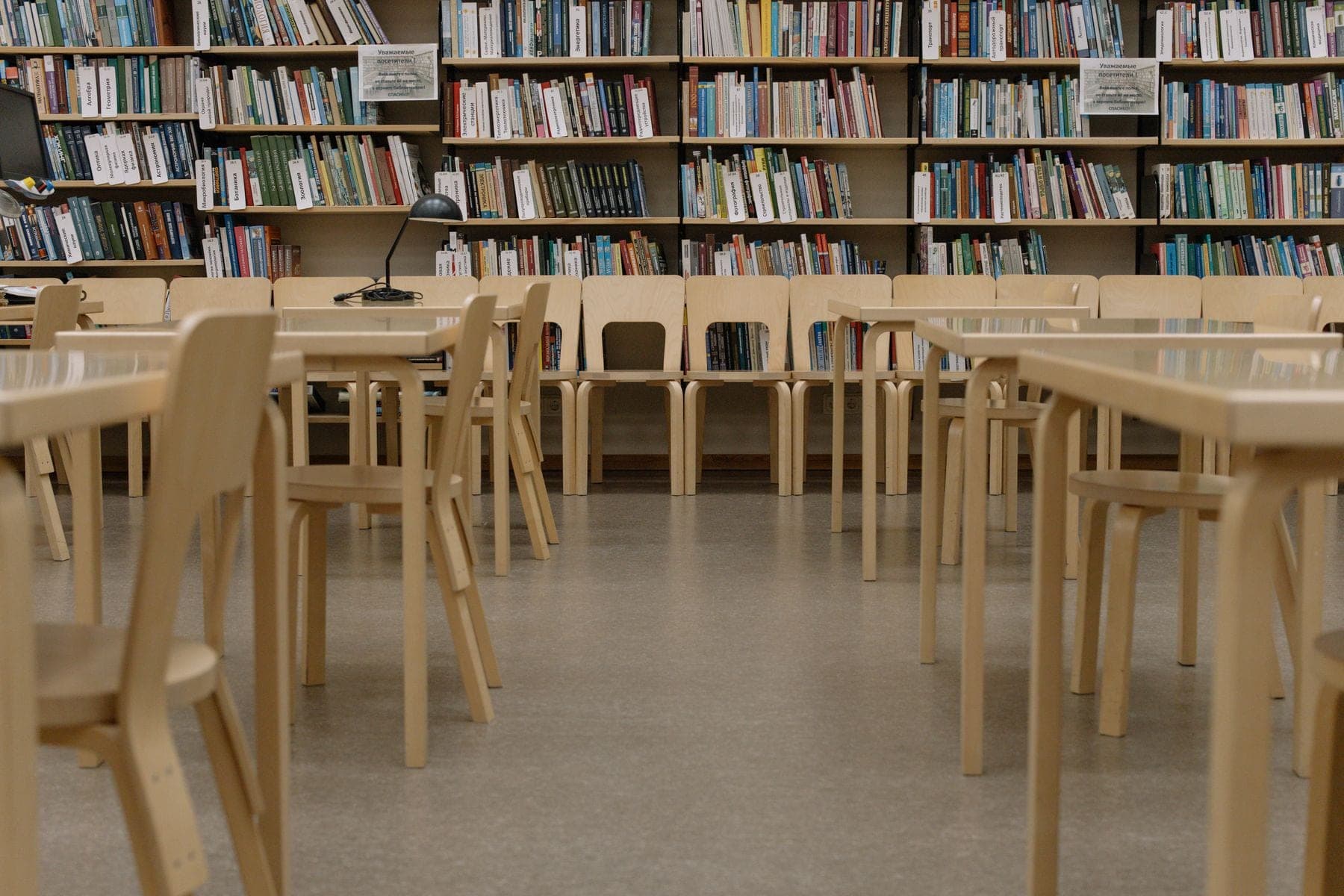 Lege houten tafels en stoelen in een universiteitsbibliotheek met volle boekenkasten