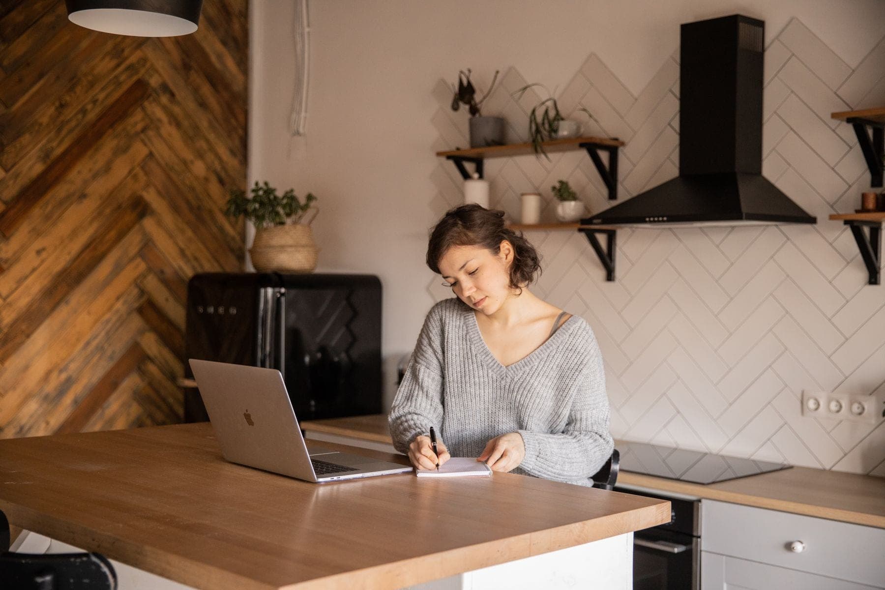 Een vrouw werkt aan de keukentafel op een laptop en maakt aantekeningen in een notitieblok